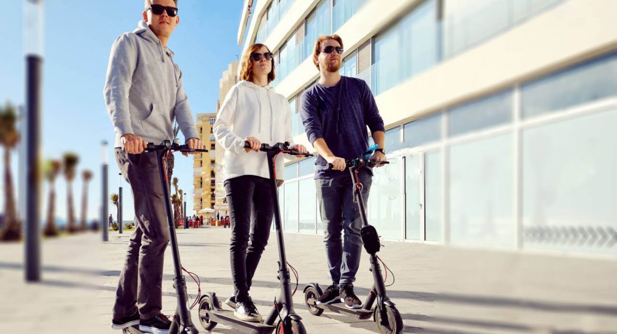 Three best friends young 20s -30s girl and guys spend time outdoors gathered together driving on electric scooter modern land vehicle, easy comfort usage, technology urban transportation concept image